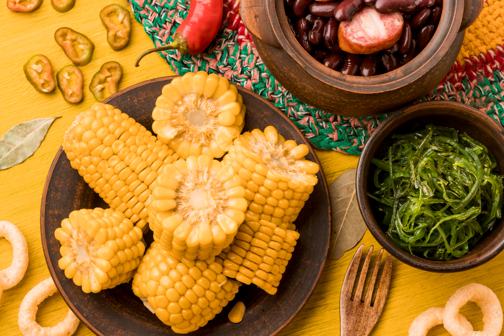 49 comidas típicas de festa junina | Milho, feijoada e couve em mesa amarela | Atacadão