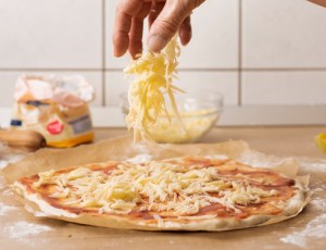 Produtos para pizzaria: o que comprar no atacado | Homem despejando queijo sobre pizza | Atacadão