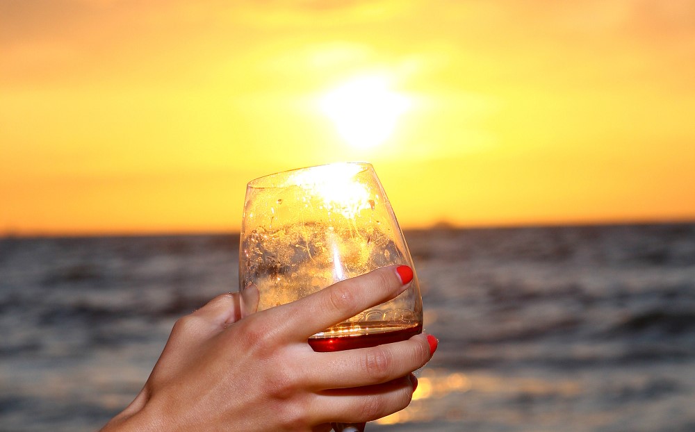 Drinks refrescantes: boas opções para o calor | Mulher segurando copo com pôr de sol ao fundo | Atacadão