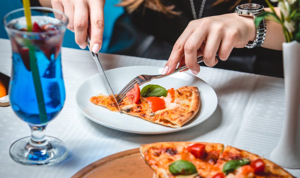 Melhores bebidas para acompanhar comida italiana | Mulher cortando pizza com drink na mesa | Atacadão