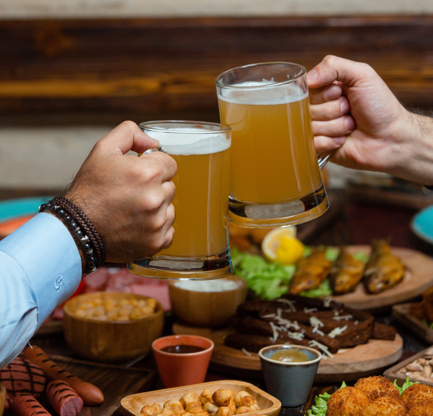 Petisco para cerveja: conheça opções deliciosas | Foto de dois homens brindando com copo de cerveja em uma mesa cheia de petiscos | Atacadão