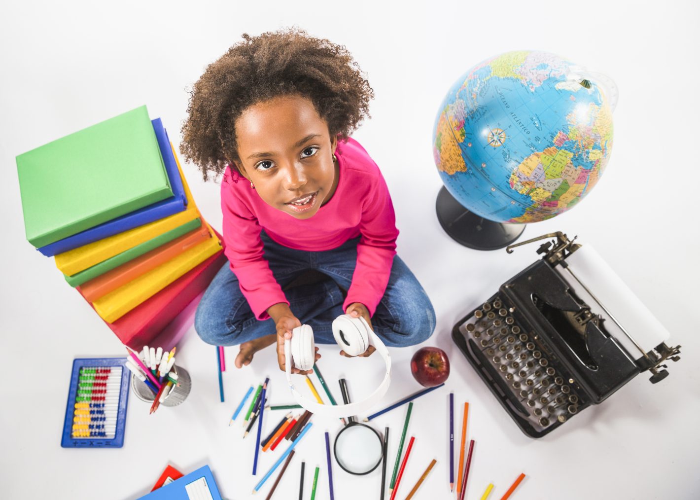 Materiais escolares: saiba como economizar na compra | Criança sentada com vários materiais escolares em volta | Atacadão