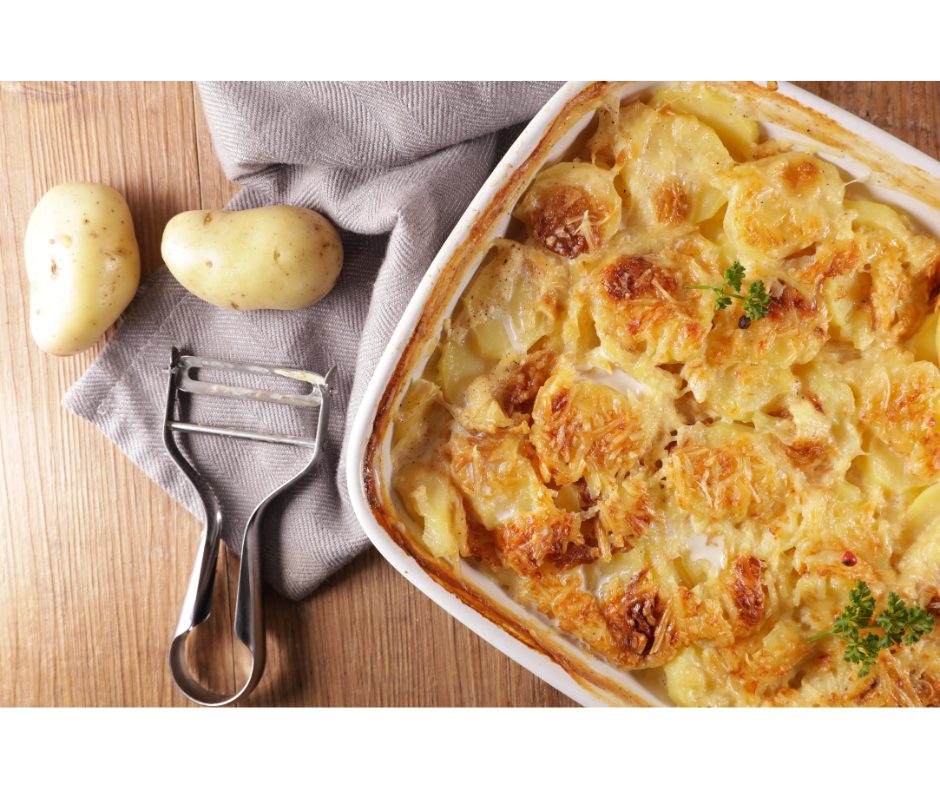 Receitas com batata: conheça duas opções | Foto superior de uma mesa com uma forma de batata gratinada, uma descascador ao lado e duas batatas com casca | Atacadão