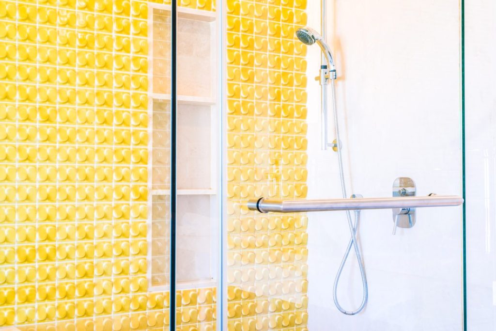 Limpeza de box de banheiro: dicas de como fazer uma limpeza eficiente | Foto de box de banheiro super limpo, na parte interna, azulejos amarelos texturizados. | Atacadão