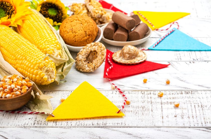5 dicas para economizar no preparo da festa junina | Foto de uma mesa com alguns doces, milhos e bandeirinhas triangulares. | Atacadão