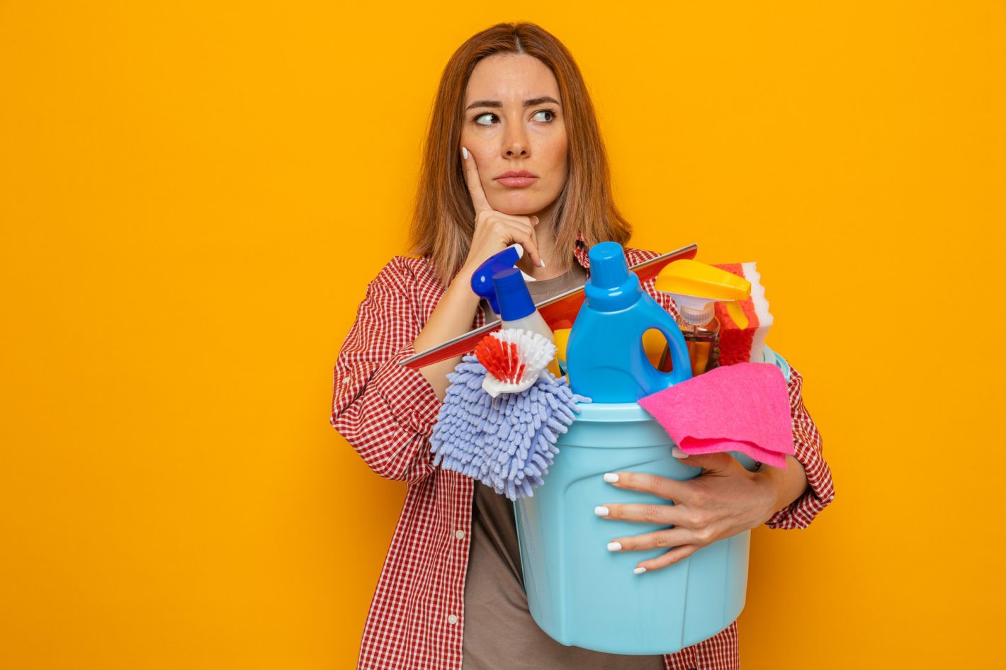 Produtos de limpeza baratos: dicas para comprar | Foto de uma mulher com expressão de dúvida, segurando um balde com produtos e objetos de limpeza. | Atacadão