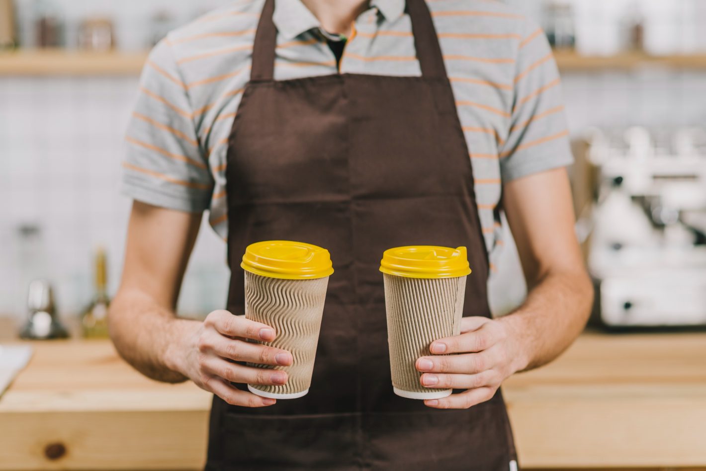 Produtos de cafeteria que valem a pena comprar por atacado | Foto do corpo de um barista segurando dois copos de café. | Atacadão