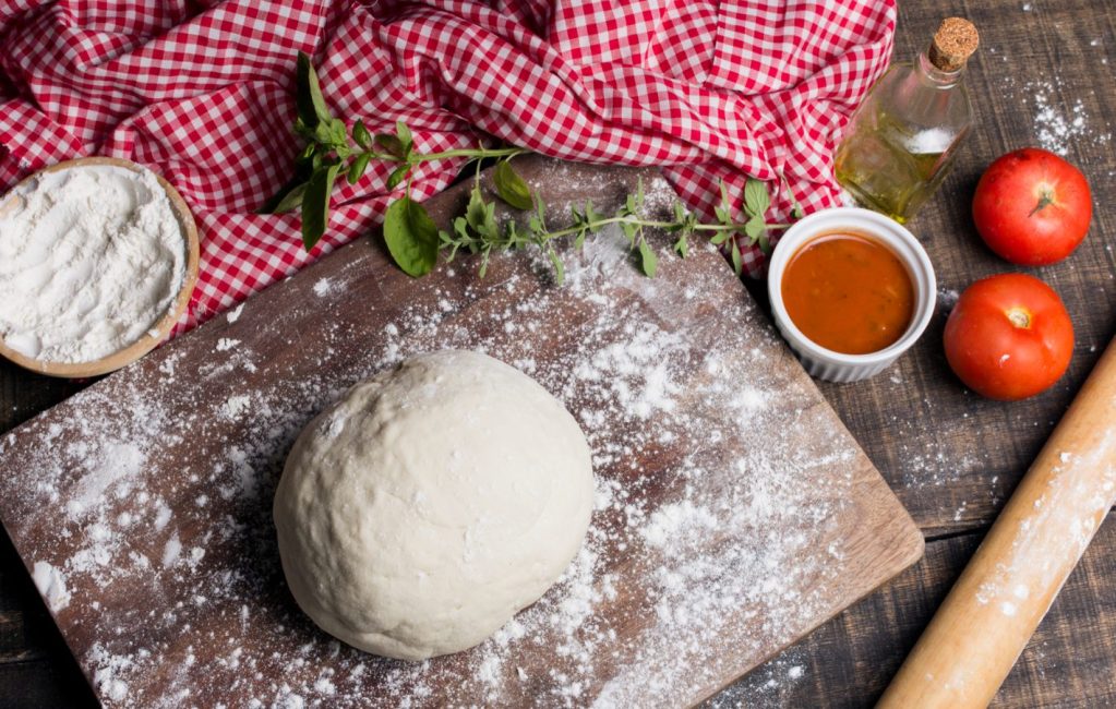 Pizza de cone: saiba como preparar | Foto superior de uma bancada com massa, molho e outros ingredientes para preparar uma pizza. | Atacadão