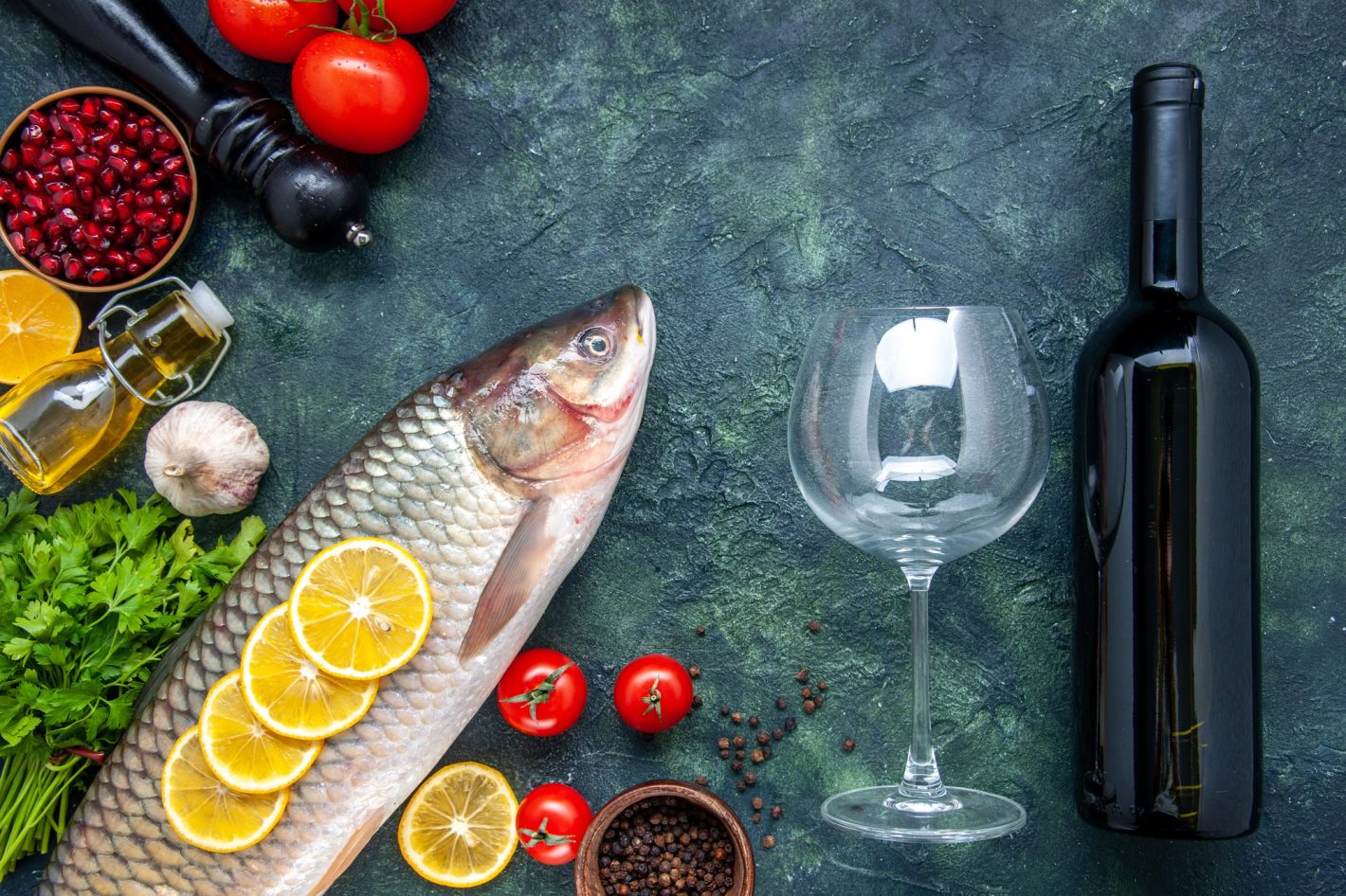Aprenda como harmonizar vinho e peixes | Foto de uma mesa com um peixe, uma garrafa de vinhos e uma taça. | Atacadão