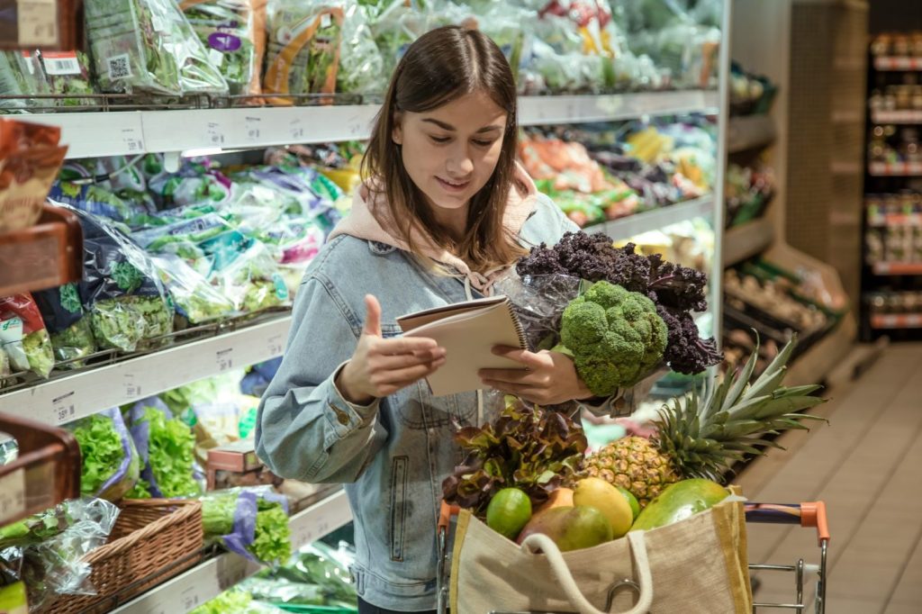 Guia para montar uma lista de compras | Foto de uma mulher com um caderno na mão, em um supermercado. | Atacadão