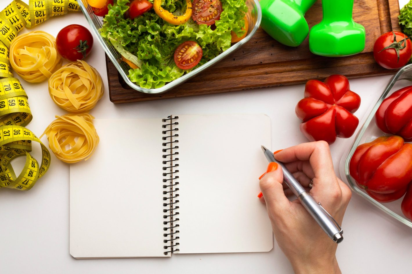 Receitas low carb: 3 dicas para sua dieta | Foto de uma mão com caderno de anotações e alguns legumes e massas em sua volta | Atacadão